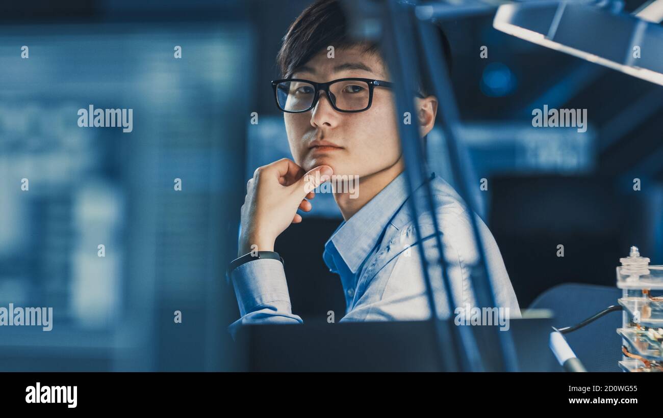 Portrait eines seriösen professionellen japanischen Entwicklungsingenieurs, der an denkt Sein Arbeitsplatz in einem High-Tech-Forschungslabor mit Moderner Computer Stockfoto