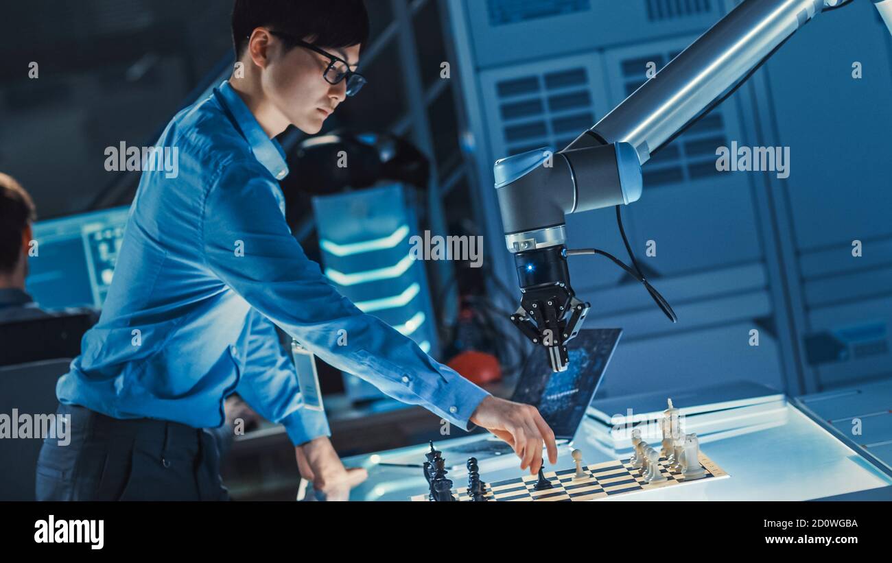 Professioneller japanischer Entwicklungsingenieur testet eine künstliche Intelligenz-Schnittstelle, indem er Schach mit einem futuristischen Roboterarm spielt. Sie sind in Stockfoto