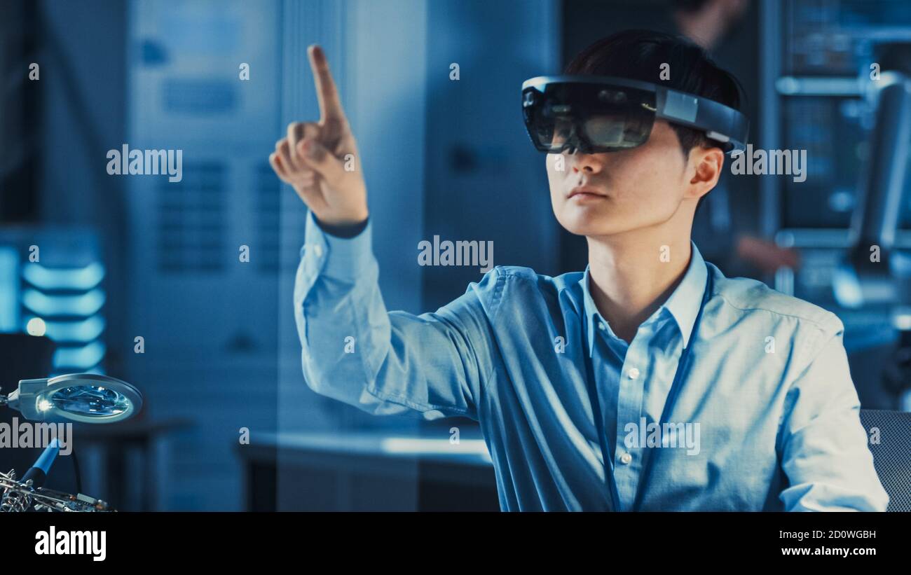 Ein professioneller japanischer Entwicklungsingenieur arbeitet in einem AR-Headset, bewegt virtuelle Teile und betrachtet Grafiken in der High-Tech-Forschung Stockfoto
