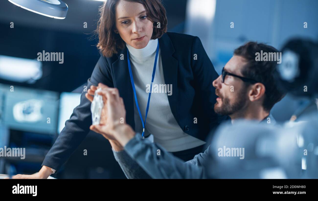 Futuristische Maschinenbauingenieurin, die am Computer an seinem Schreibtisch arbeitet, spricht mit weiblicher Projektmanagerin. Team von Fachleuten, die in arbeiten Stockfoto