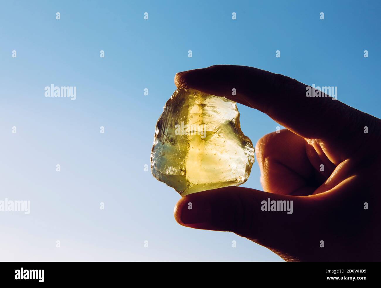 Person Hand hält eine gelb grüne Zitrone Quarzkristall Stein gegen Sonne und blauen Himmel. Glänzend, Kopierbereich. Stockfoto