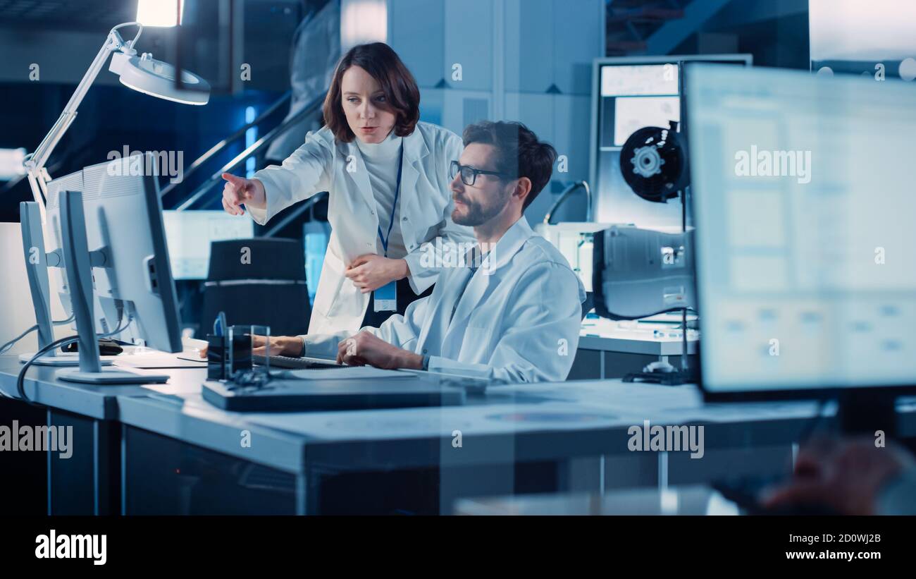 Entwicklungsingenieur für Maschinenmotoren, der an seinem Schreibtisch am Computer arbeitet, spricht mit dem Projektmanager und zeigt Prototyp-Komponente. Team von Fachleuten Stockfoto