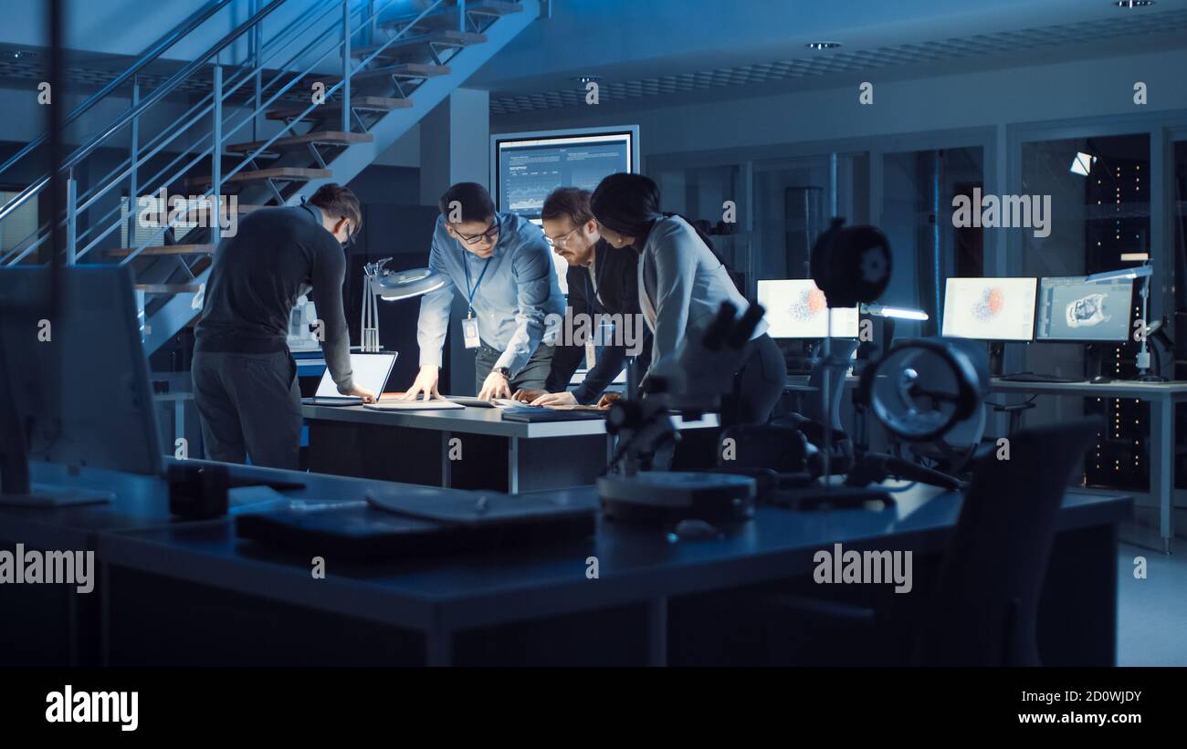 Vielfältiges Team von Elektronikentwicklern, die am Schreibtisch stehen und mit Dokumenten arbeiten, um Projektprobleme spät in der Nacht zu lösen. Spezialisten Stockfoto