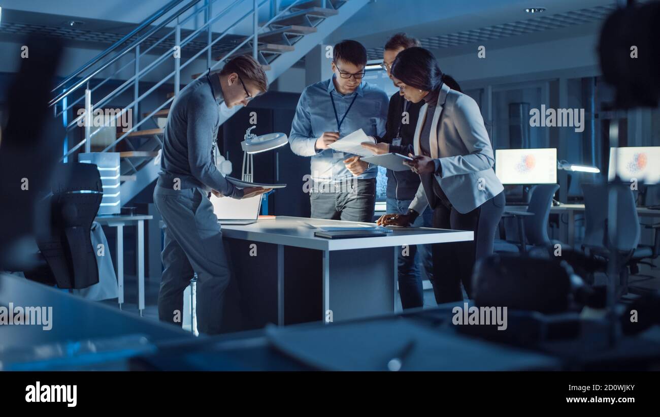 Ein vielfältiges Team von Elektronikentwicklern, das am Schreibtisch steht und Projektprobleme spät in der Nacht erfolgreich löst, feiert mit High Five Stockfoto