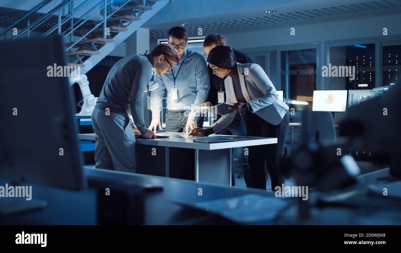 Vielfältiges Team von Elektronikentwicklern, die am Schreibtisch stehen und mit Dokumenten arbeiten, um Projektprobleme spät in der Nacht zu lösen. Spezialisten Stockfoto