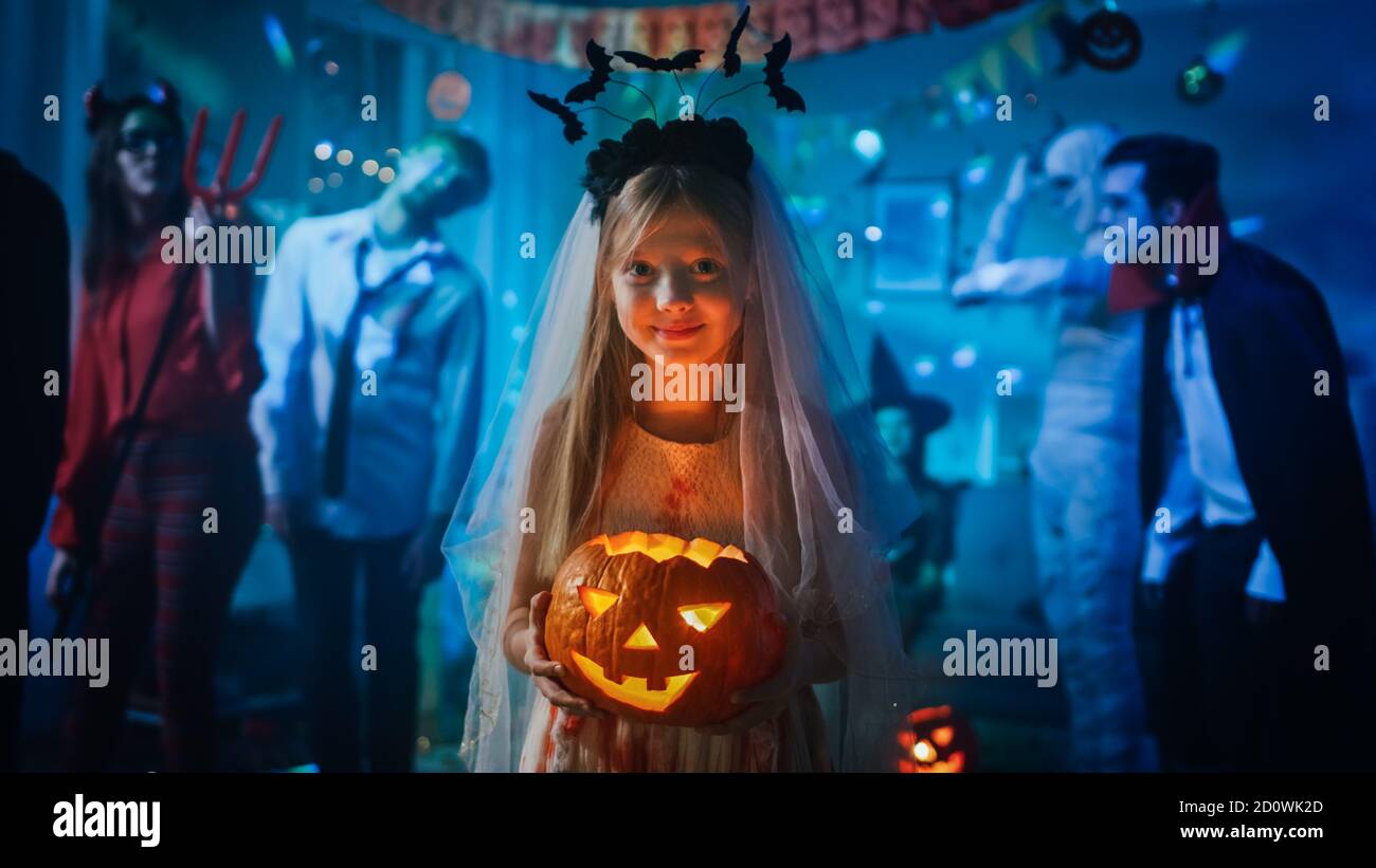 Halloween Kostüm Party: Lächelndes kleines Mädchen in einem blutigen weißen Brautkleid mit brennenden Kürbis Kopf. Zombie, Blutrünstige Dracula, Mama Stockfoto