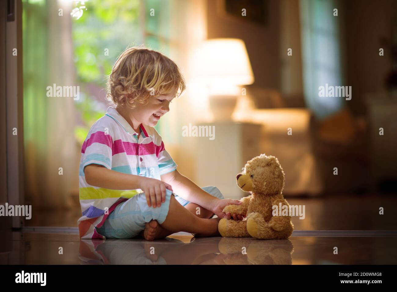 Kind, das mit Teddybär spielt. Kleiner Junge umarmt sein Lieblingsspielzeug. Kind und gestopftes Tier zu Hause. Kleinkind sitzt auf dem Boden des Wohnzimmers mit B. Stockfoto