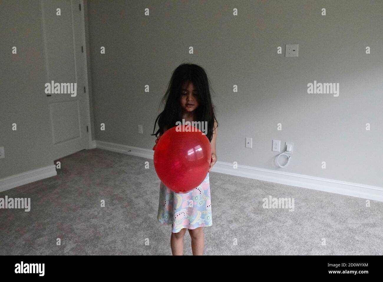 Fünf Jahre altes Mädchen spielt mit einem roten Ballon in Ein leerer Raum Stockfoto