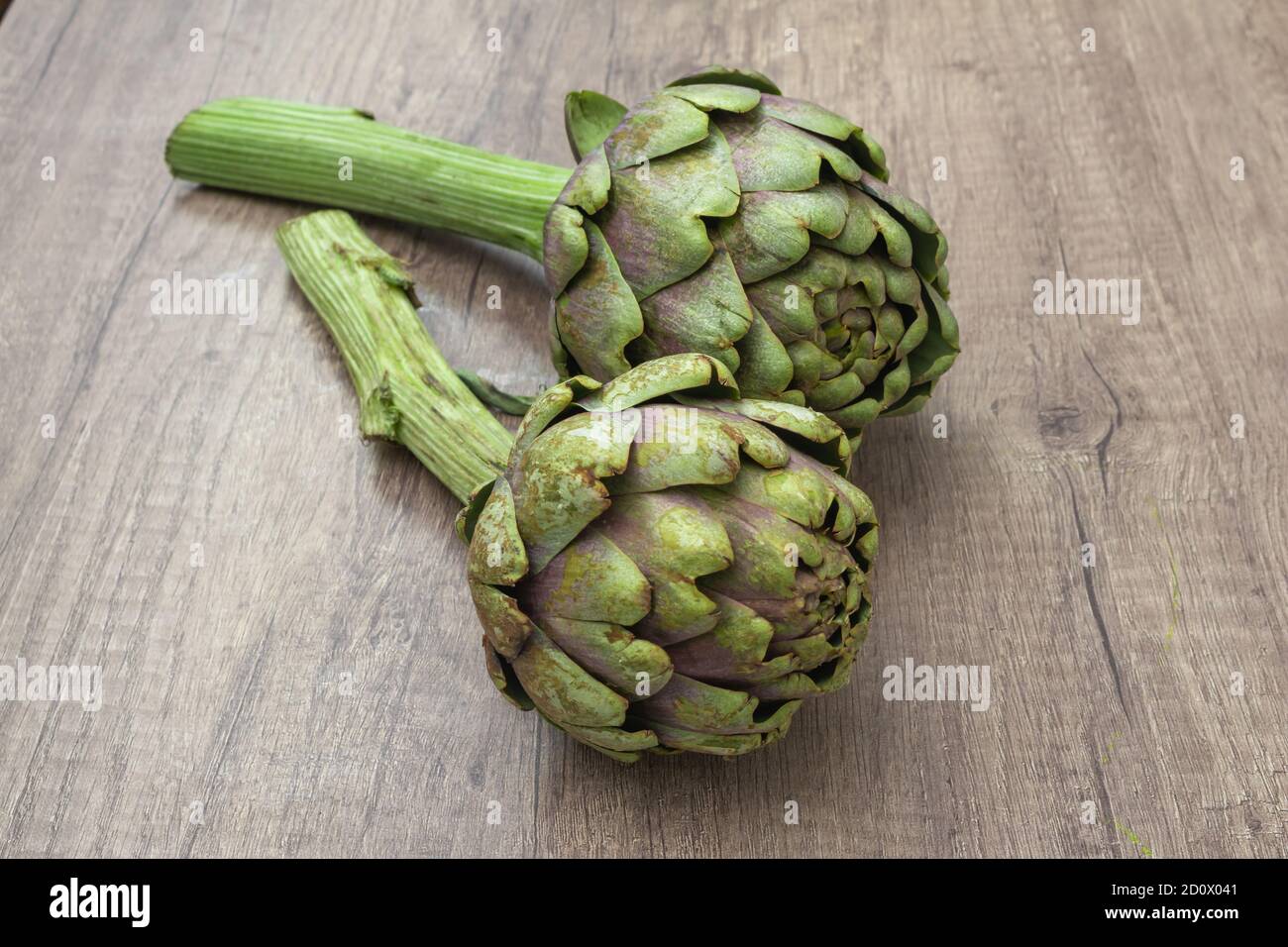 Zwei frische Bio-lila Artischocken mit Stiel Akzente auf einem Rustikale Holzoberfläche Stockfoto