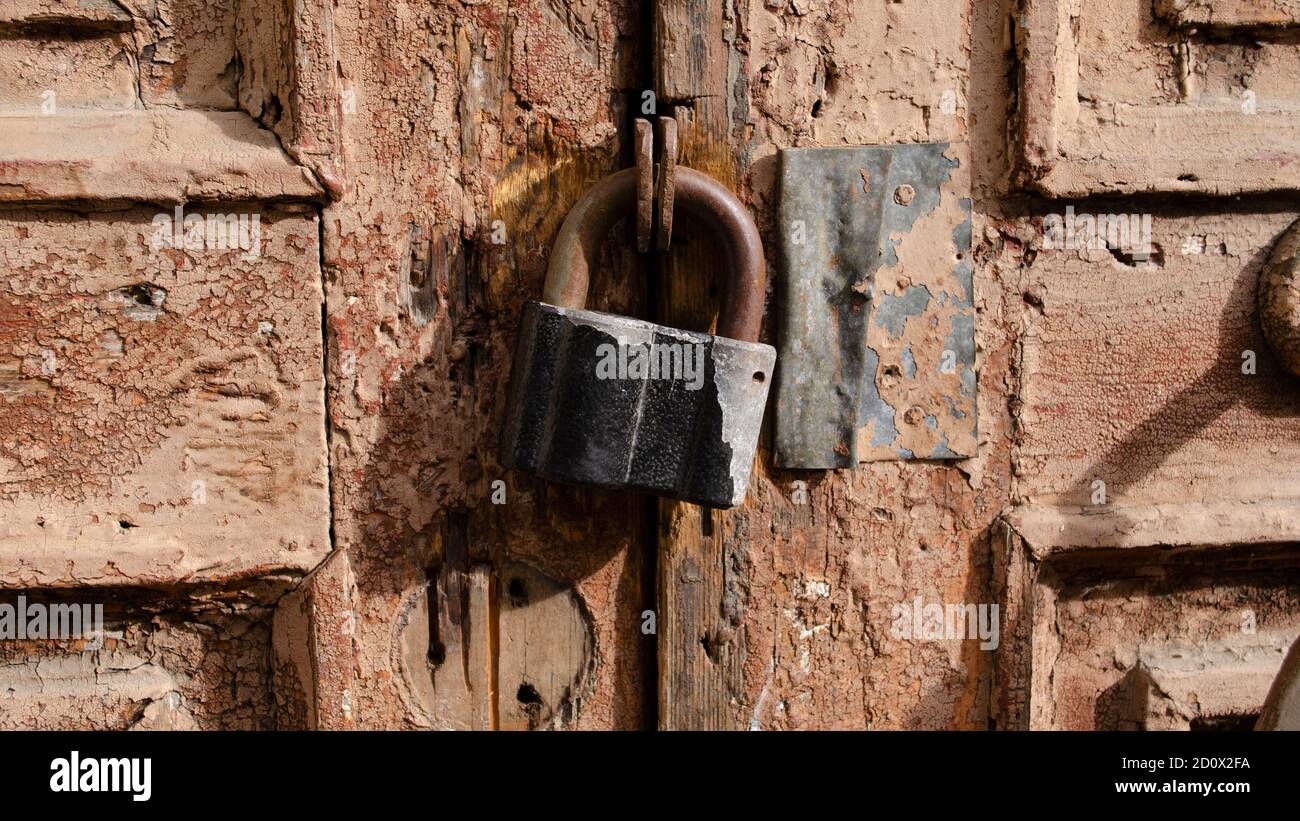 Das Schloss an der alten Holztür schloss sich. Rost auf dem Metallschloss. Die braune Farbe blättert an der alten Tür ab. Uralte Textur. Stockfoto