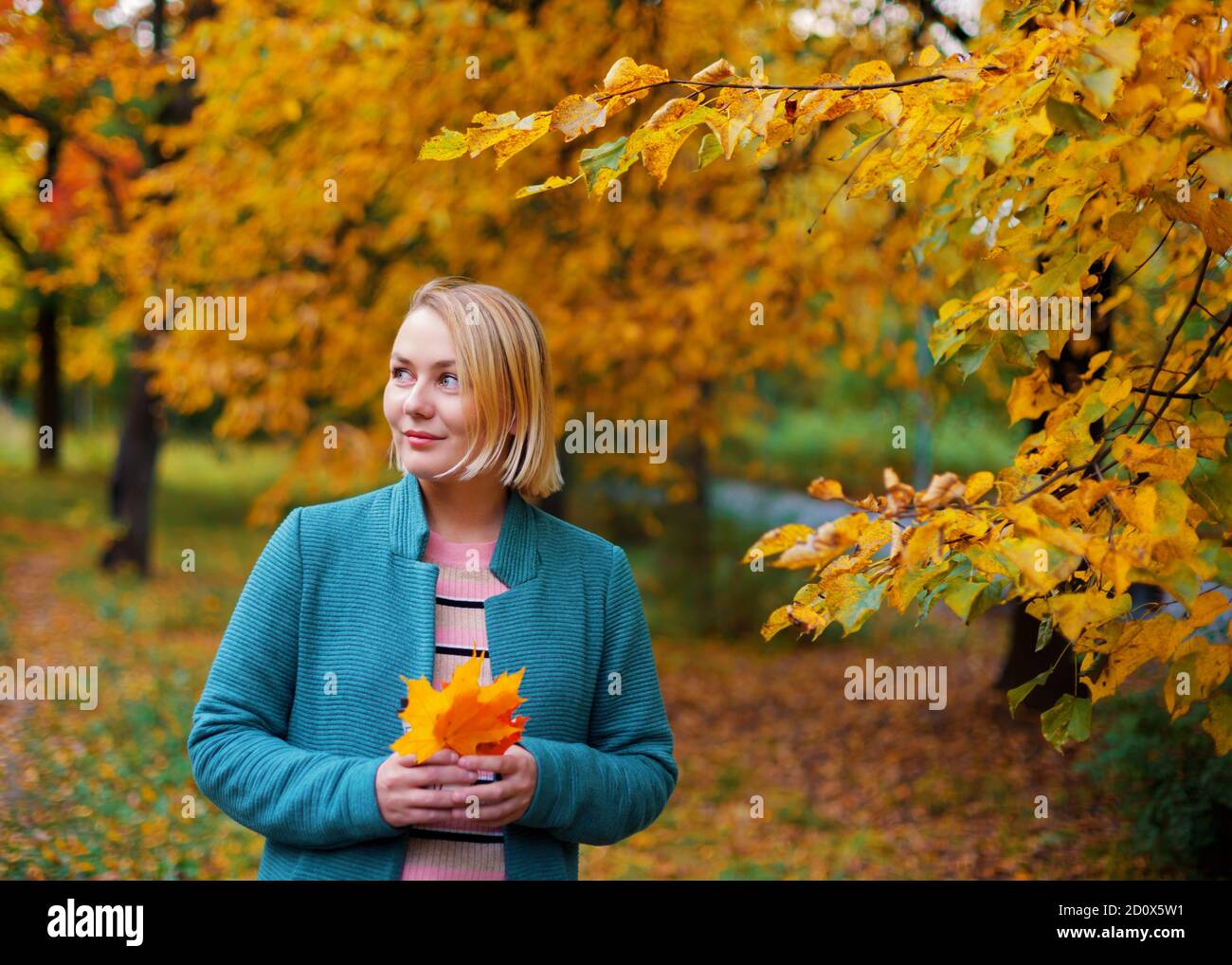 Schöne blonde Frau lächelt und schaut auf der linken Seite mit Ahornblättern in den Händen. Stockfoto