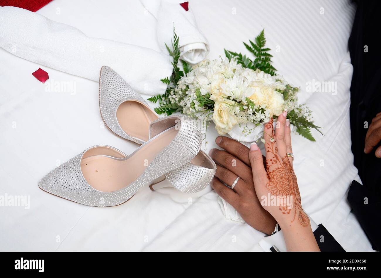 Ein Bräutigam hält die Hand der Braut. Die Hand der Braut ist mit Henna-Tattoos verziert. Im Hintergrund ein Blumenstrauß Stockfoto