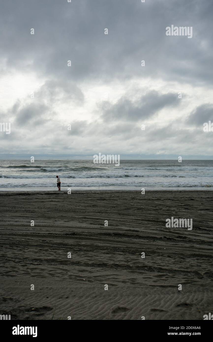Ein einsamer Mann zu Fuß über den Strand mit einem dramatischen Stürmischer Himmel über dem Horizont Stockfoto