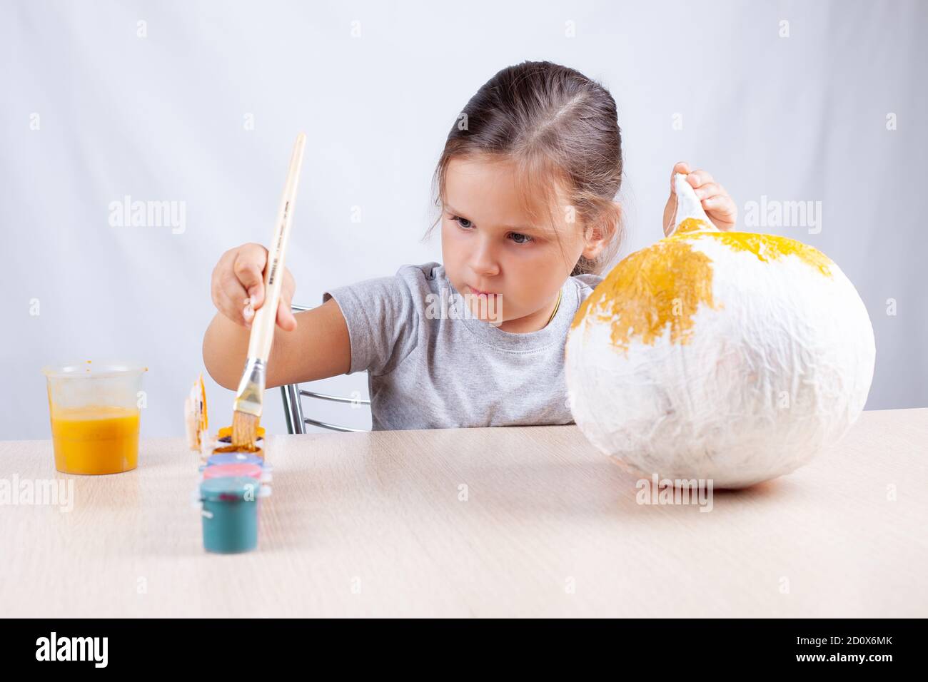Ein Kind taucht einen Pinsel in Farbe, um einen hausgemachten Kürbis für Halloween, ein Hobby zur Selbstisolation, zu dekorieren Stockfoto