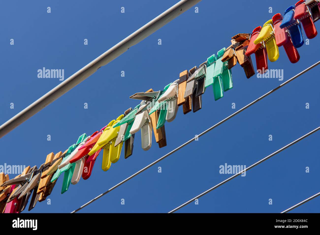 Eine farbige Kleidung hängt an einem Trockengestell Draht. Eine Gruppe von Wäscheklammern in der Linie gegen den blauen Himmel. Stockfoto