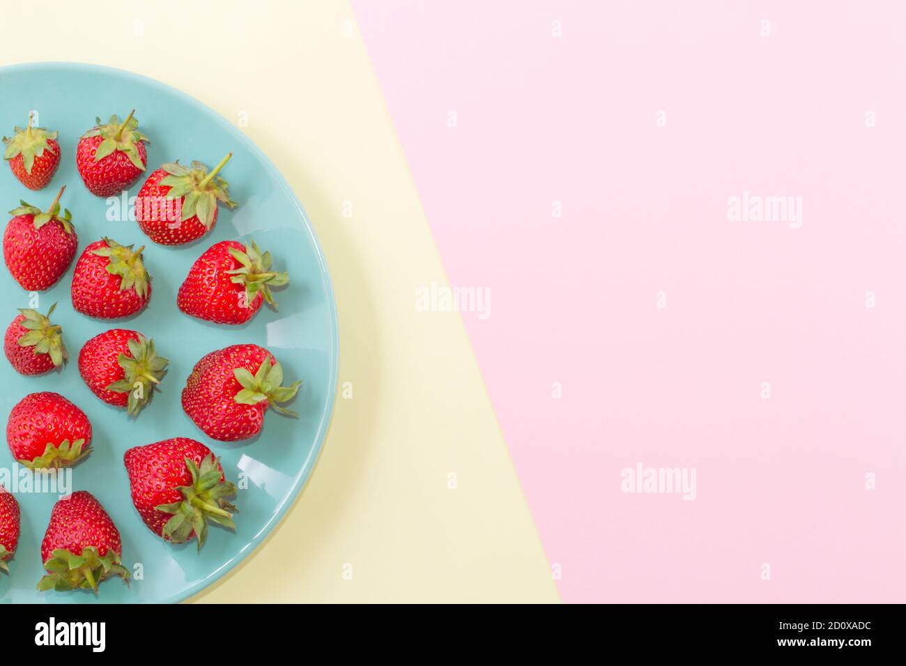 Helle Reifen saftigen Erdbeeren auf einem Pastell türkis Platte auf einem doppelten Pastell rosa-gelben Hintergrund. Stockfoto