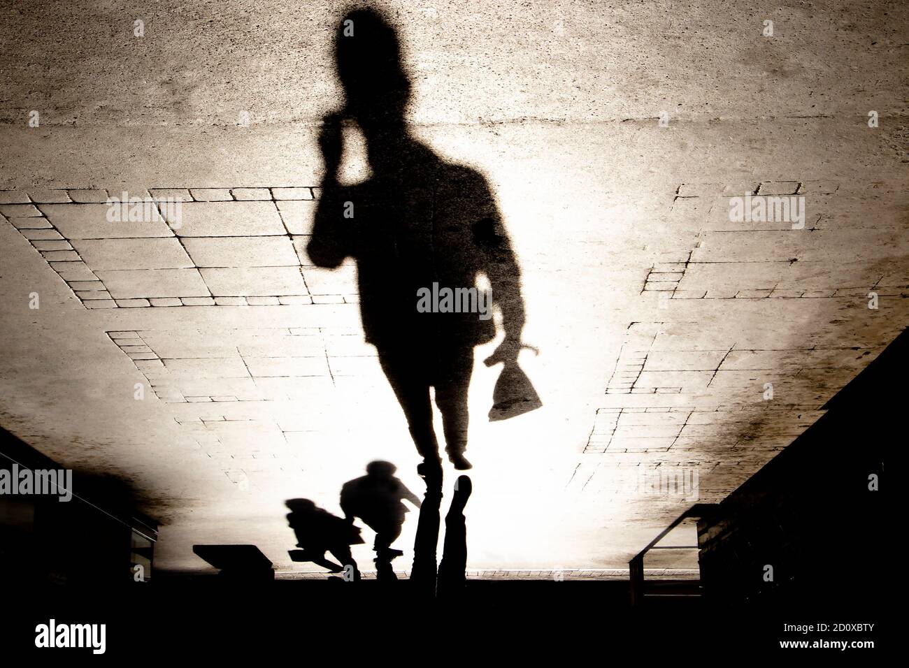 Verschwommene Schattensilhouette eines Mannes, der am Telefon spricht Und zu Fuß Fußgängerzone, während kleine Tasche in Sepia Schwarz und Weiß mit hohem Kontrast Stockfoto