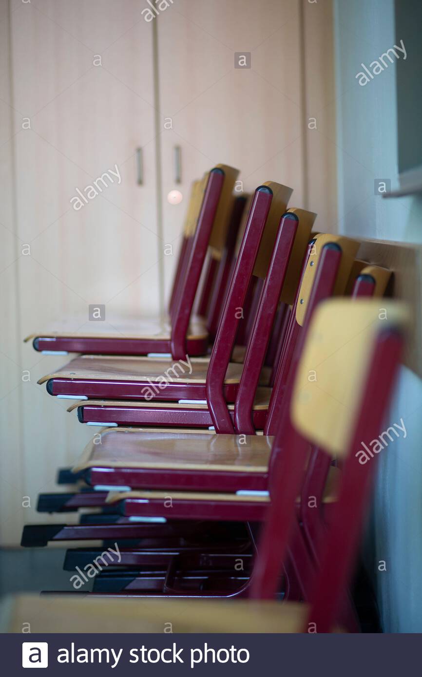 Ungenutzte rote Stühle in der Ecke eines Klassenzimmers gestapelt In Deutschland Stockfoto