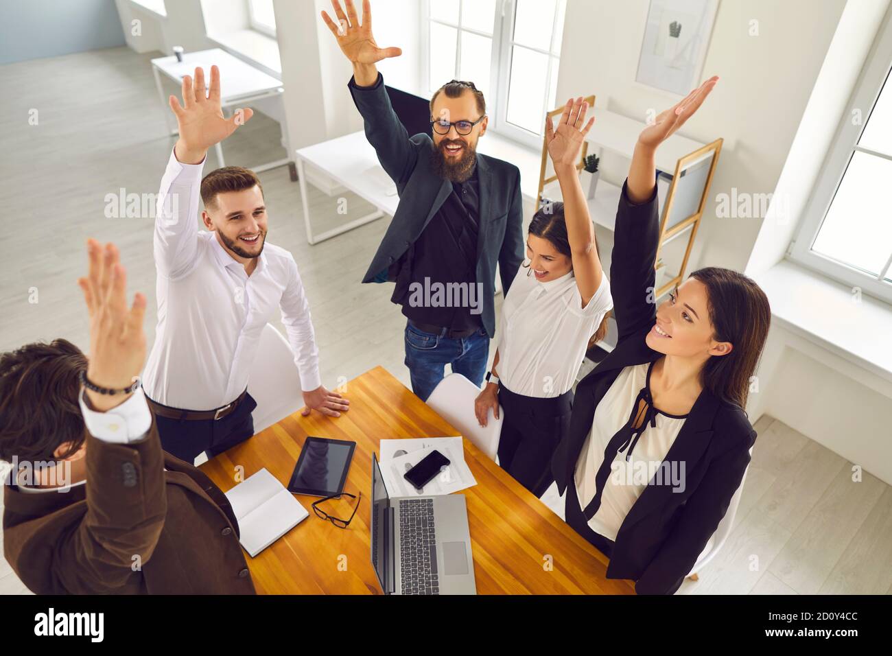 Team von enthusiastischen Geschäftsleuten, die bei der Arbeitssitzung Waffen erheben Erfolgreiche Teamarbeit feiern Stockfoto