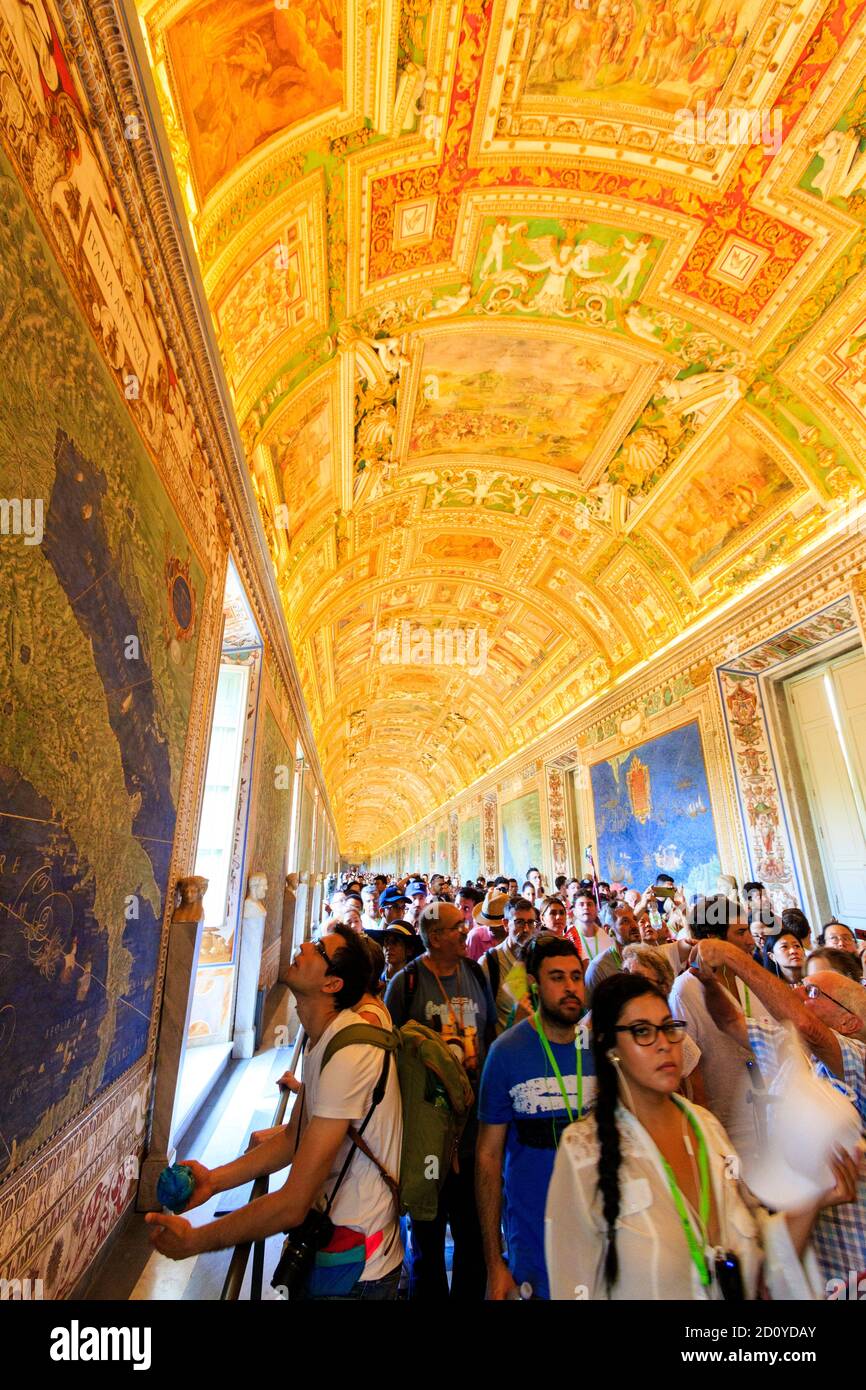 Die Menschen drängten sich in die Galerie der Landkarten im Vatikanischen Museum. Weitwinkelansicht mit verzierten Deckenmalereien und großen Stoffkarten an den Wänden. Stockfoto