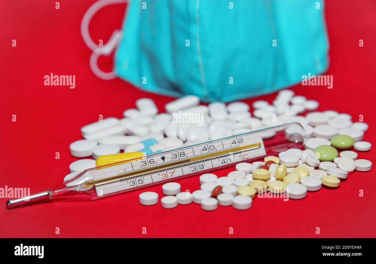 Schutzmaske, Medikamente und Thermometer auf rotem Hintergrund. Stockfoto