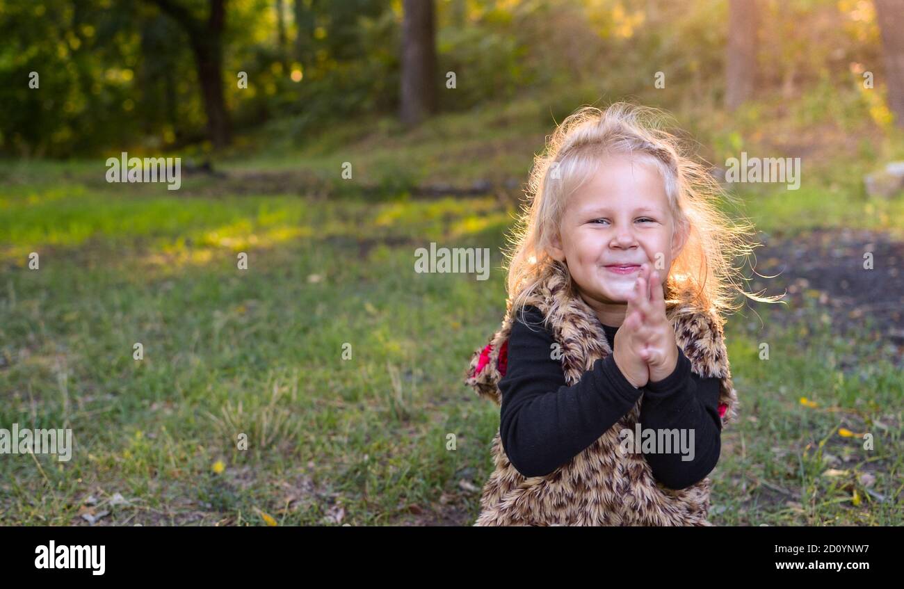 Kinderportrait, Nahaufnahme. Mädchen im Freien in der Natur. Schönes Mädchen 3 Jahre alt. Herbstfoto. Das Baby klatscht in die Hände und lächelt kindliche Emotionen. Stockfoto