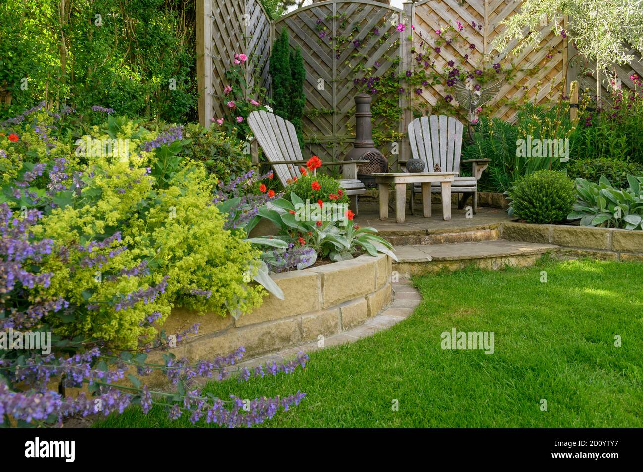 Landschaftlich schöner, sonniger privater Garten (modernes Design, farbenfrohe Sommerblumen, Randpflanzen, Sitzmöbel auf der Terrasse, Rasen) - Yorkshire, England, Großbritannien Stockfoto