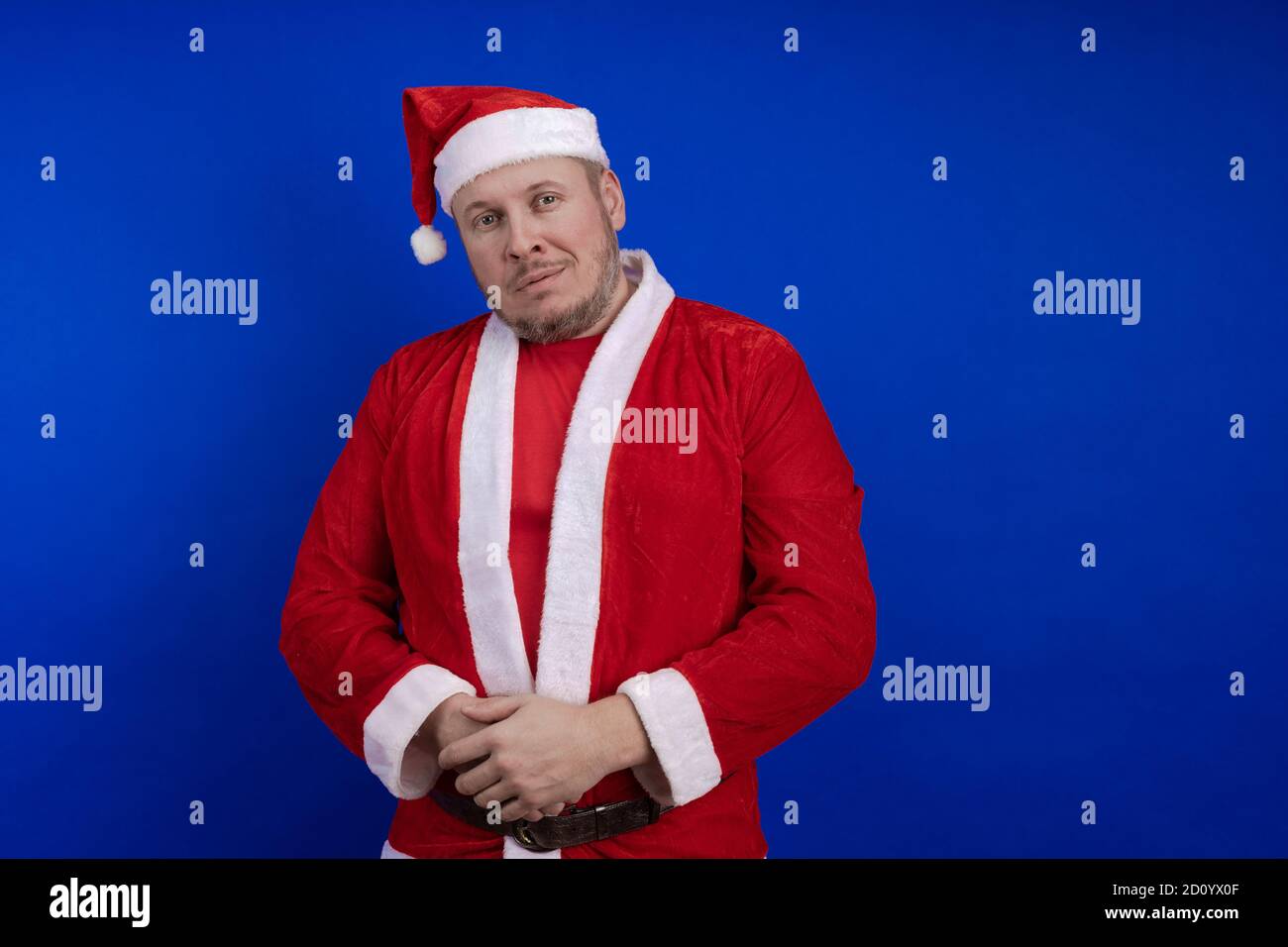 Männlicher Schauspieler in Kostüm und Hut des Weihnachtsmannes posiert auf blauem Hintergrund. Stockfoto