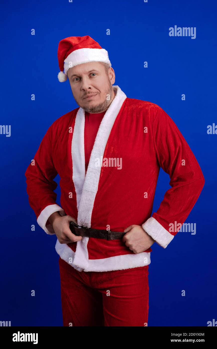 Männlicher Schauspieler in Kostüm und Hut des Weihnachtsmannes posiert auf blauem Hintergrund. Stockfoto