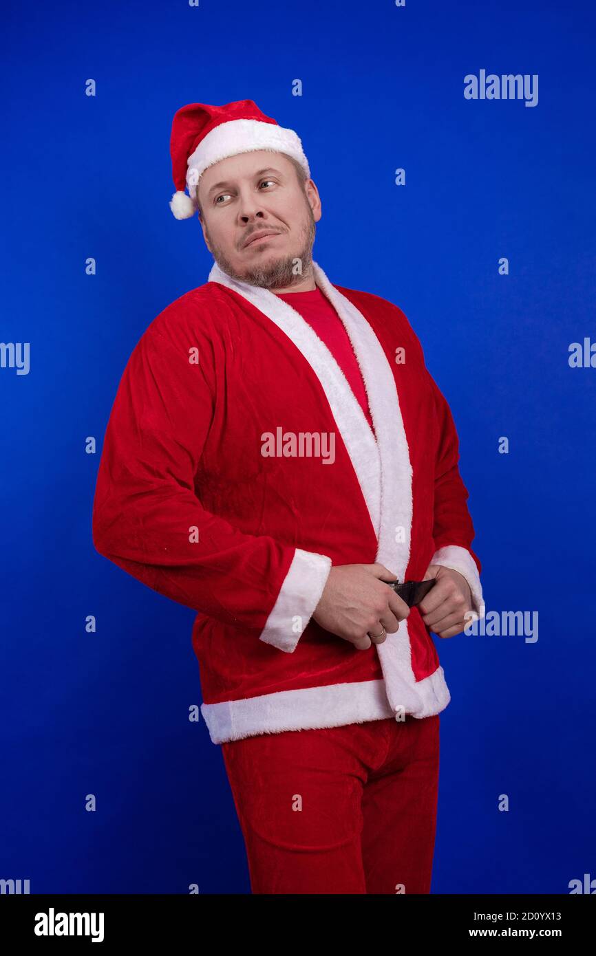 Männlicher Schauspieler in Kostüm und Hut des Weihnachtsmannes posiert auf blauem Hintergrund. Stockfoto