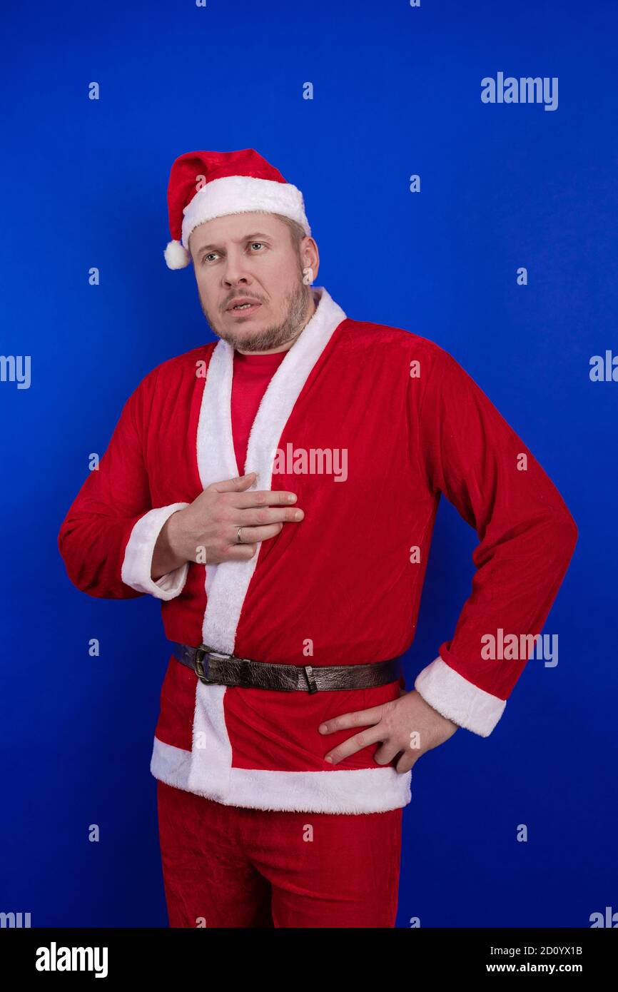 Männlicher Schauspieler in Kostüm und Hut des Weihnachtsmannes posiert auf blauem Hintergrund. Stockfoto