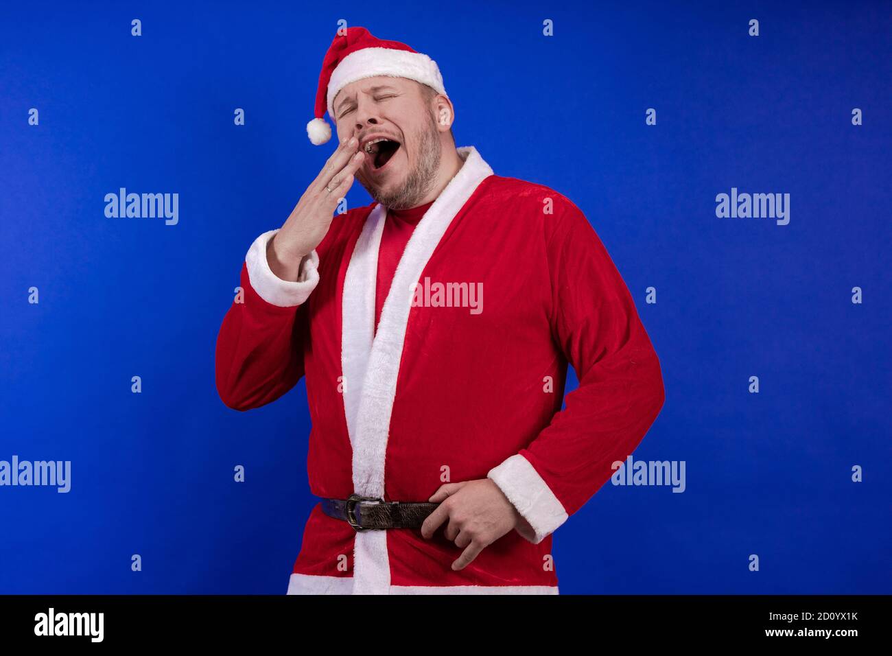 Männlicher Schauspieler in Kostüm und Hut des Weihnachtsmannes posiert auf blauem Hintergrund. Stockfoto