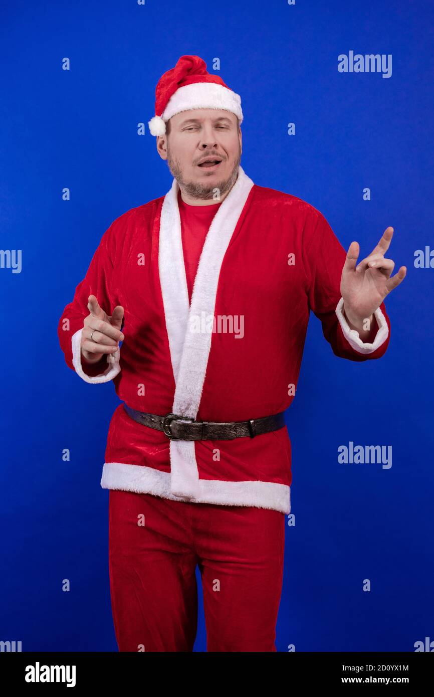 Männlicher Schauspieler in Kostüm und Hut des Weihnachtsmannes posiert auf blauem Hintergrund. Stockfoto