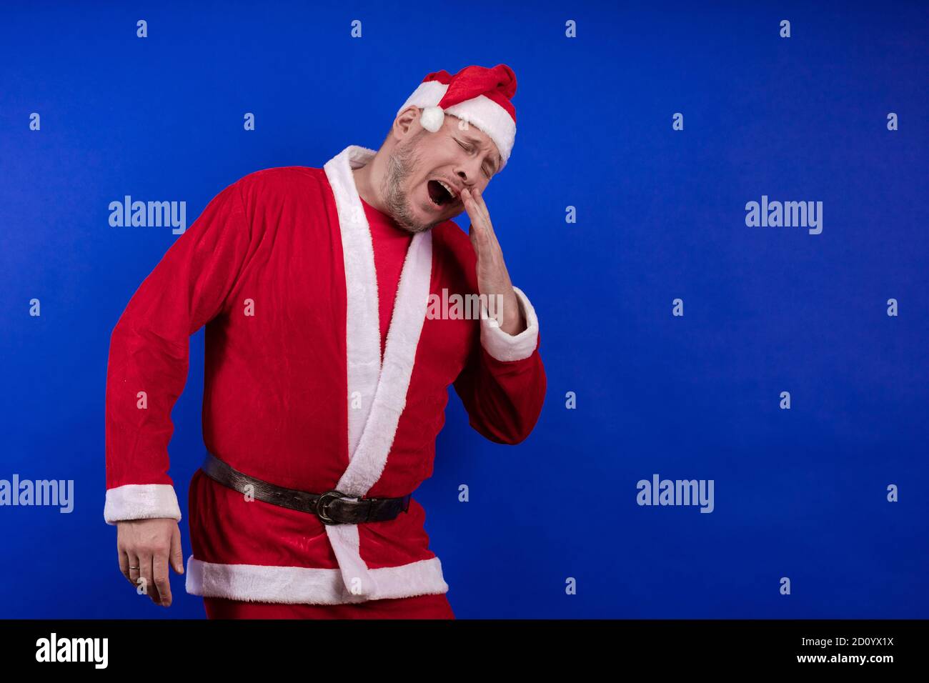 Männlicher Schauspieler in Kostüm und Hut des Weihnachtsmannes posiert auf blauem Hintergrund. Stockfoto