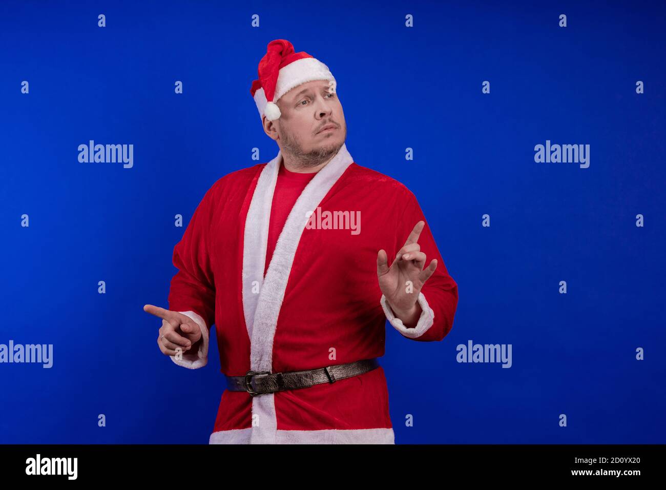 Männlicher Schauspieler in Kostüm und Hut des Weihnachtsmannes posiert auf blauem Hintergrund. Stockfoto
