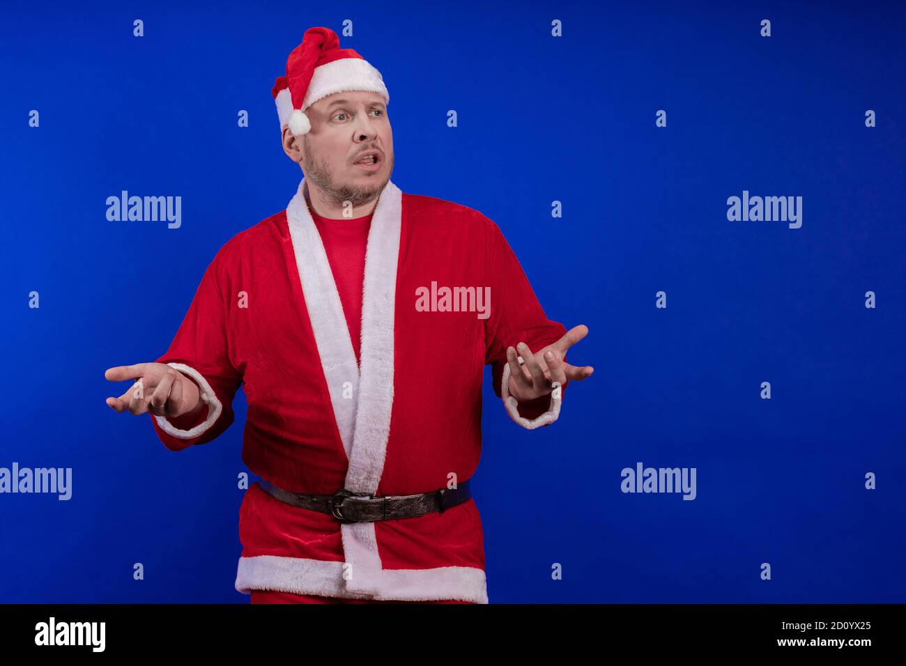 Männlicher Schauspieler in Kostüm und Hut des Weihnachtsmannes posiert auf blauem Hintergrund. Stockfoto