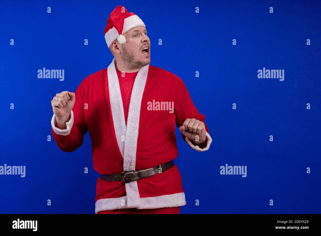 Männlicher Schauspieler in Kostüm und Hut des Weihnachtsmannes posiert auf blauem Hintergrund. Stockfoto