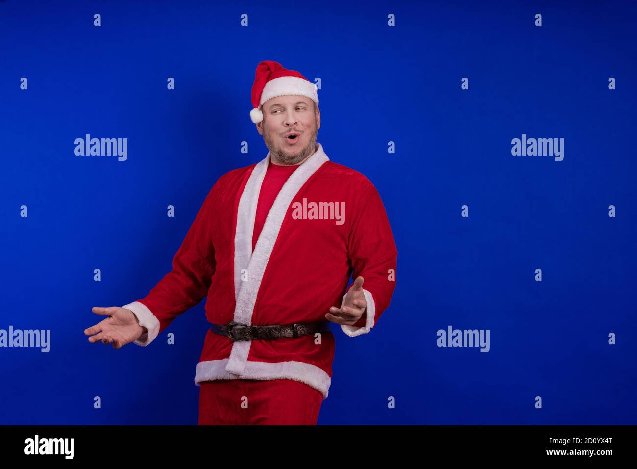 Männlicher Schauspieler in Kostüm und Hut des Weihnachtsmannes posiert auf blauem Hintergrund. Stockfoto