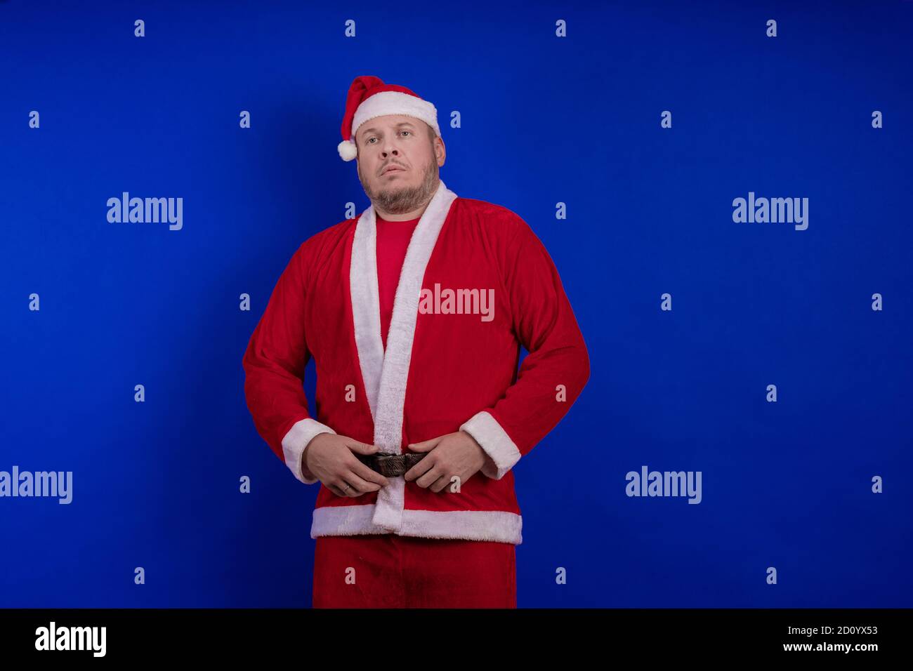Männlicher Schauspieler in Kostüm und Hut des Weihnachtsmannes posiert auf blauem Hintergrund. Stockfoto