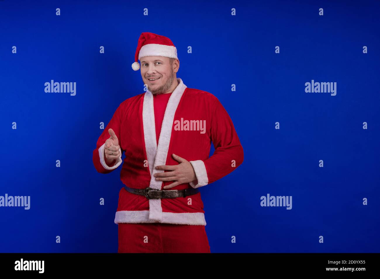 Männlicher Schauspieler in Kostüm und Hut des Weihnachtsmannes posiert auf blauem Hintergrund. Stockfoto