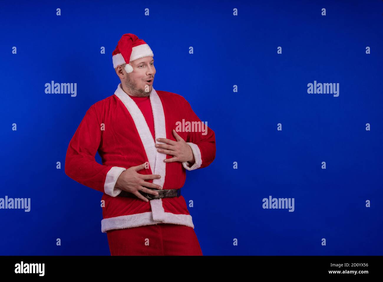 Männlicher Schauspieler in Kostüm und Hut des Weihnachtsmannes posiert auf blauem Hintergrund. Stockfoto