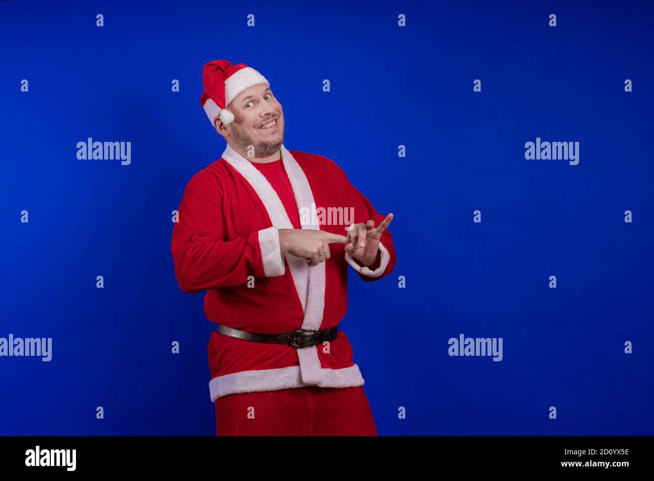 Männlicher Schauspieler in Kostüm und Hut des Weihnachtsmannes posiert auf blauem Hintergrund. Stockfoto