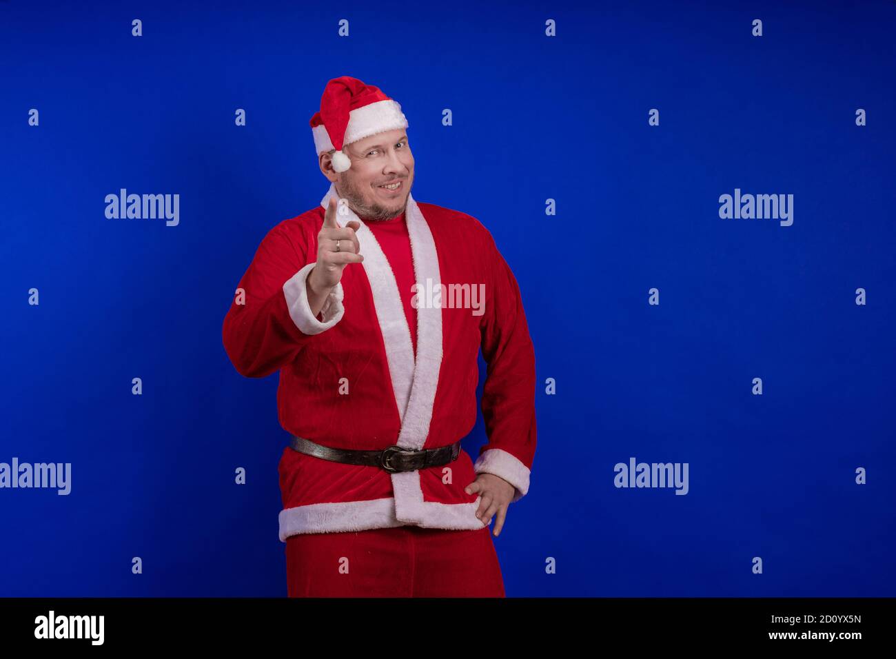 Männlicher Schauspieler in Kostüm und Hut des Weihnachtsmannes posiert auf blauem Hintergrund. Stockfoto