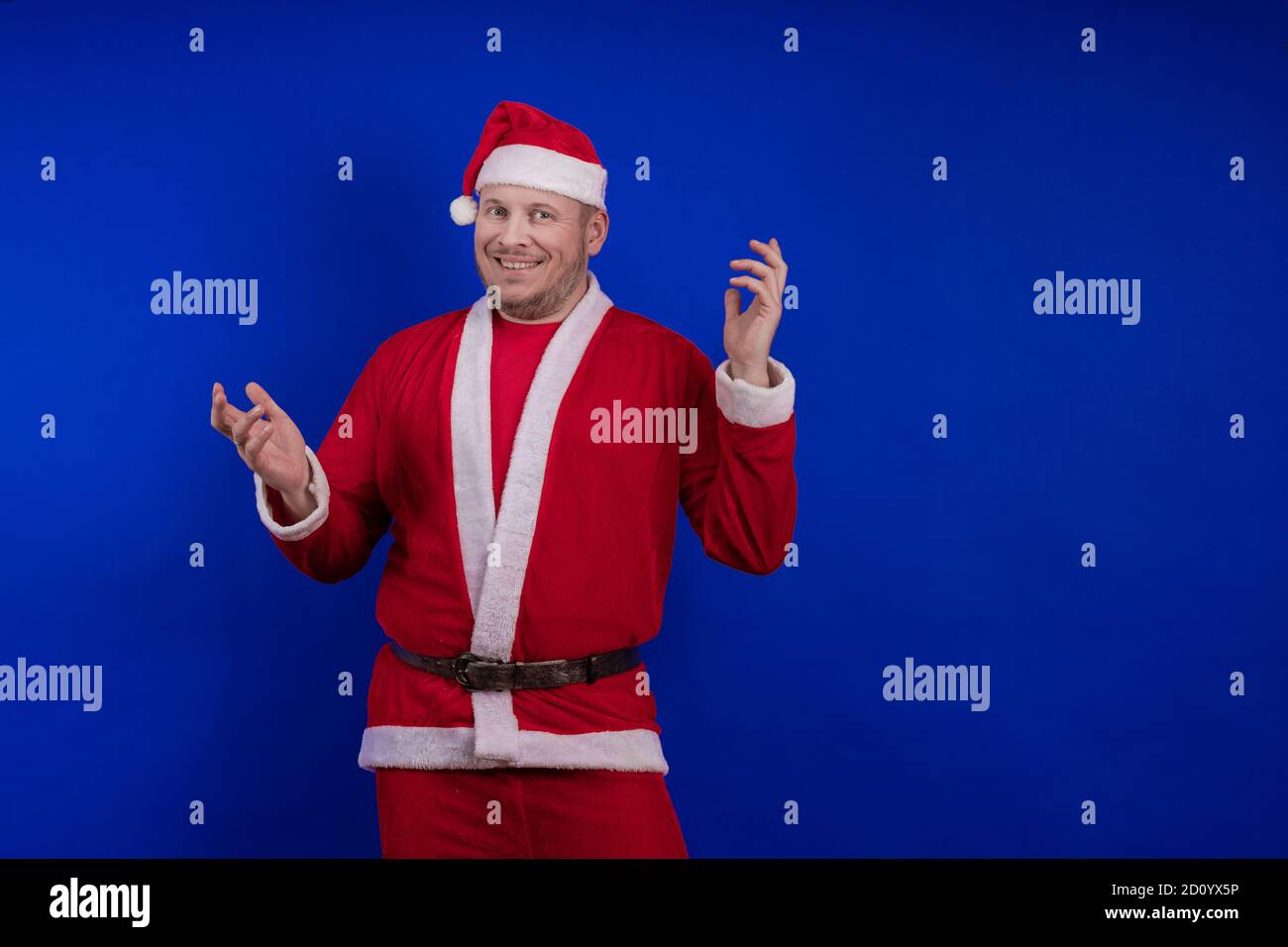 Männlicher Schauspieler in Kostüm und Hut des Weihnachtsmannes posiert auf blauem Hintergrund. Stockfoto