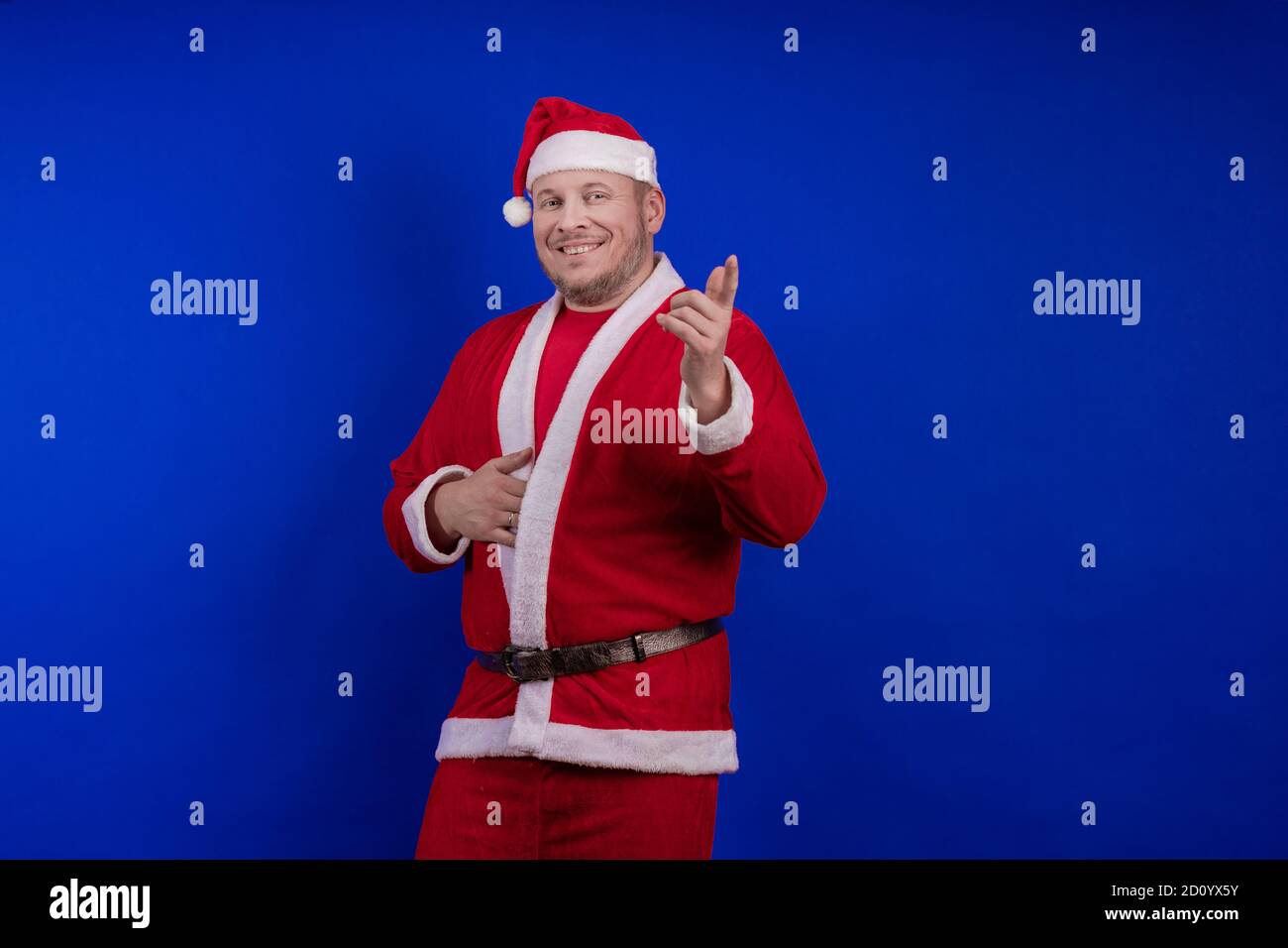 Männlicher Schauspieler in Kostüm und Hut des Weihnachtsmannes posiert auf blauem Hintergrund. Stockfoto