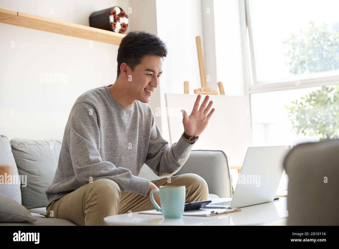 Glücklich und lächelnd junge asiatische Geschäftsführer von zu Hause aus arbeiten Begrüßung von Kollegen oder Kunden während des Meetings mit Videoanruf Stockfoto
