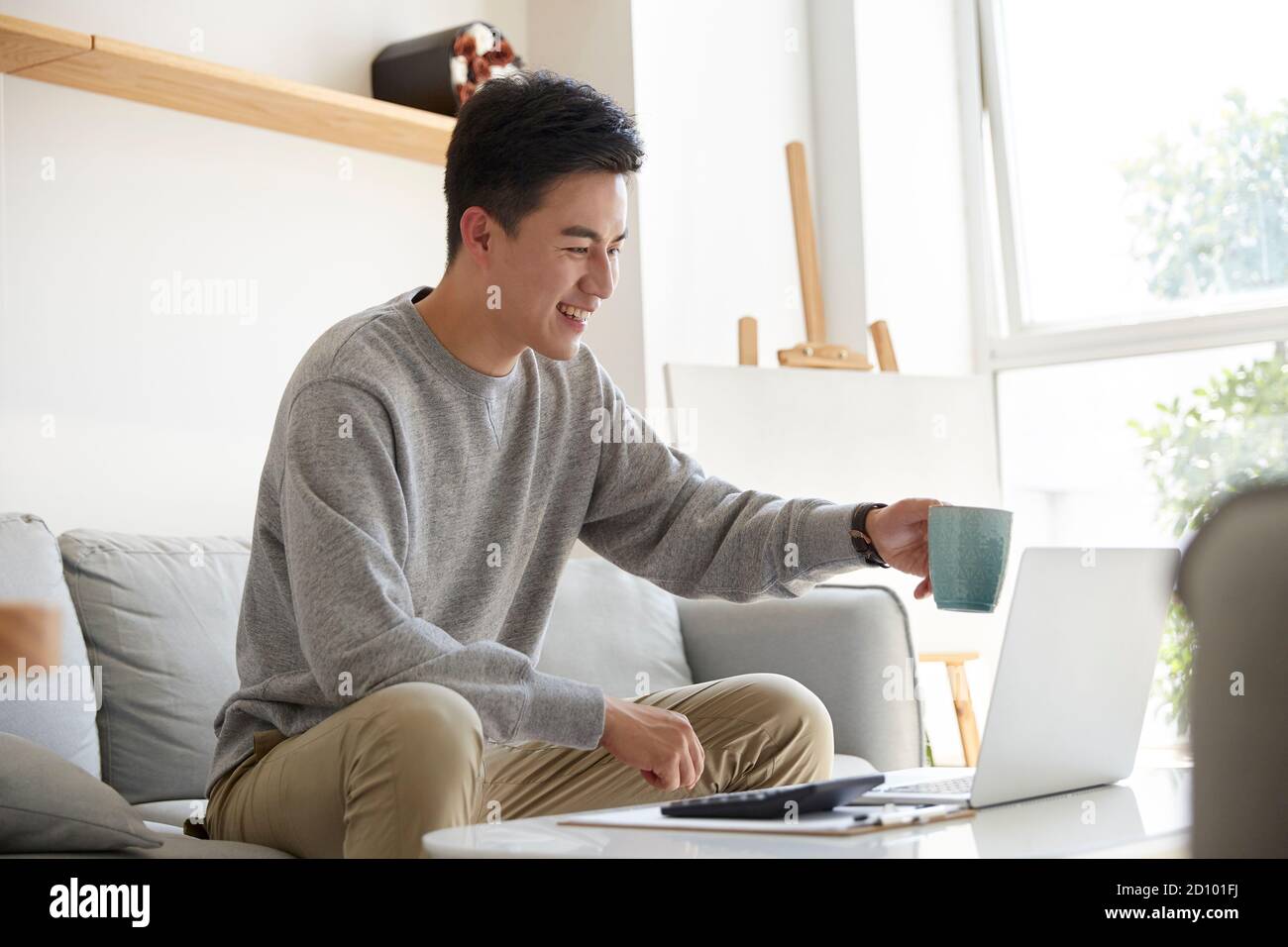 Glücklich und lächelnd junge asiatische Geschäftsführer von zu Hause aus arbeiten Vorschlagen eines Toasts während eines Meetings mit Kollegen oder Kunden mit Videoanruf Stockfoto