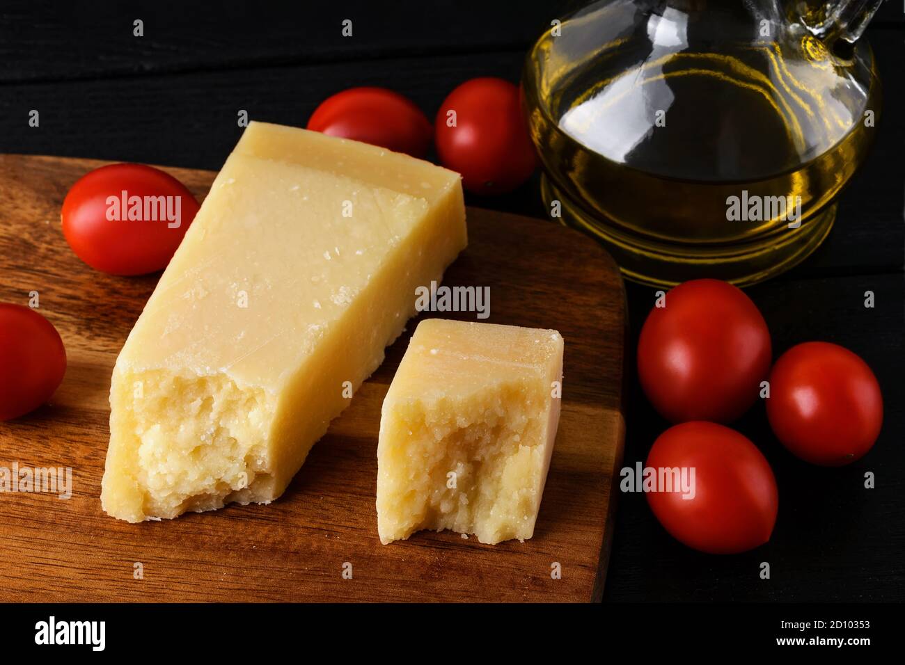 Keil aus italienischem Hartkäse Parmesan oder Grana Padano auf einem braunen Holzschneidebad, kleinen roten Tomaten und Olivenöl. Low-Key-Bild. Stockfoto