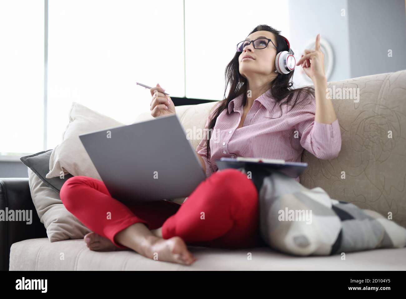 Frau mit Kopfhörer sitzen auf der Couch, hören Audio und merken sich Text. Stockfoto
