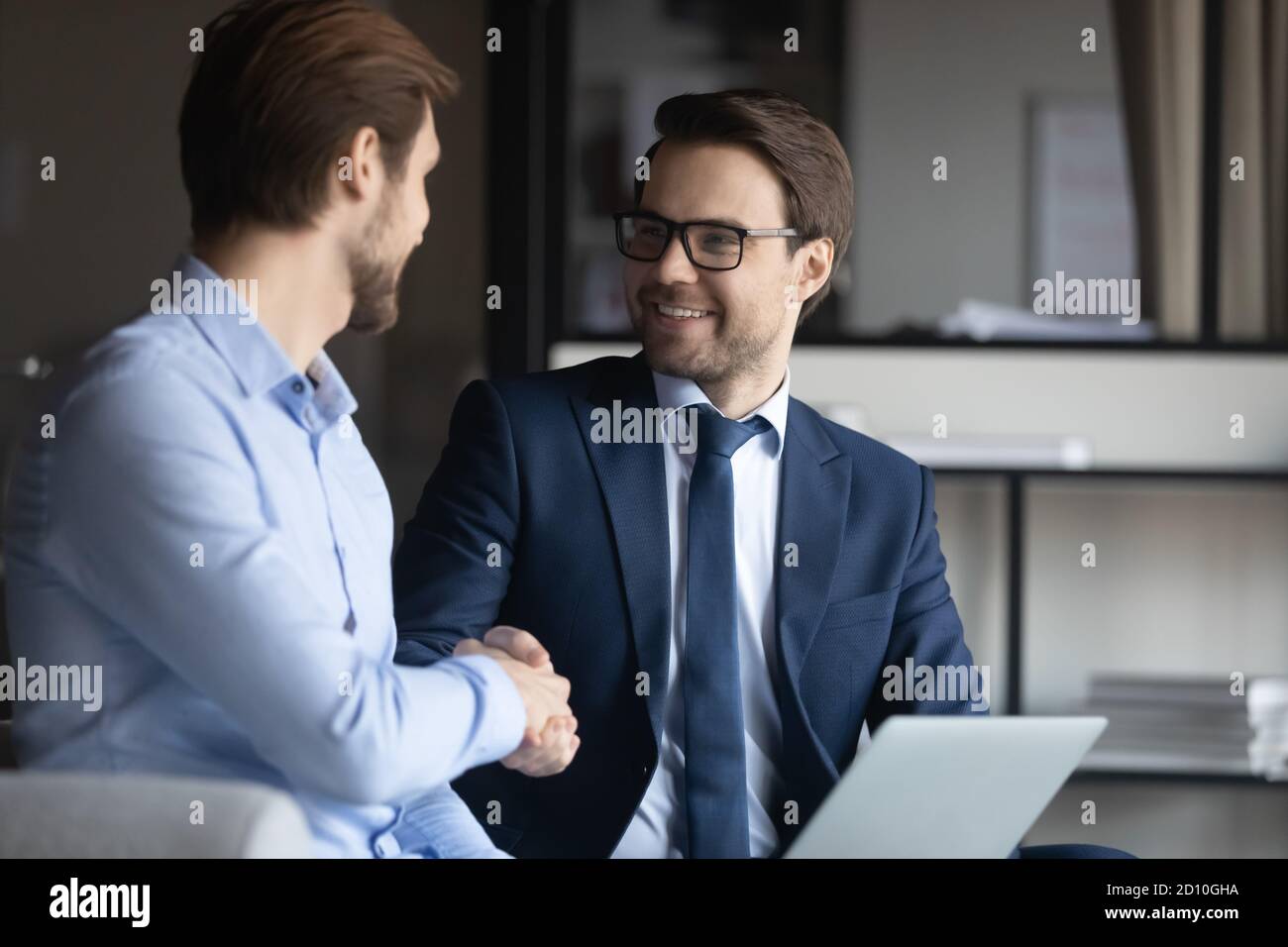 Lächelnder Geschäftsmann in Brillen und Anzug Hände schüttelnd mit Partner. Stockfoto